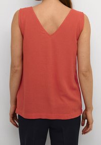 Coral sleeveless top with a V-back design, made of lightweight fabric. Features a relaxed fit and a straight hemline, paired with navy trousers.