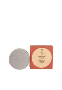 Balsamo solido in argento, con forma rotonda. Scatola di colore ruggine con un'etichetta circolare, che presenta i dettagli del prodotto in beige chiaro.