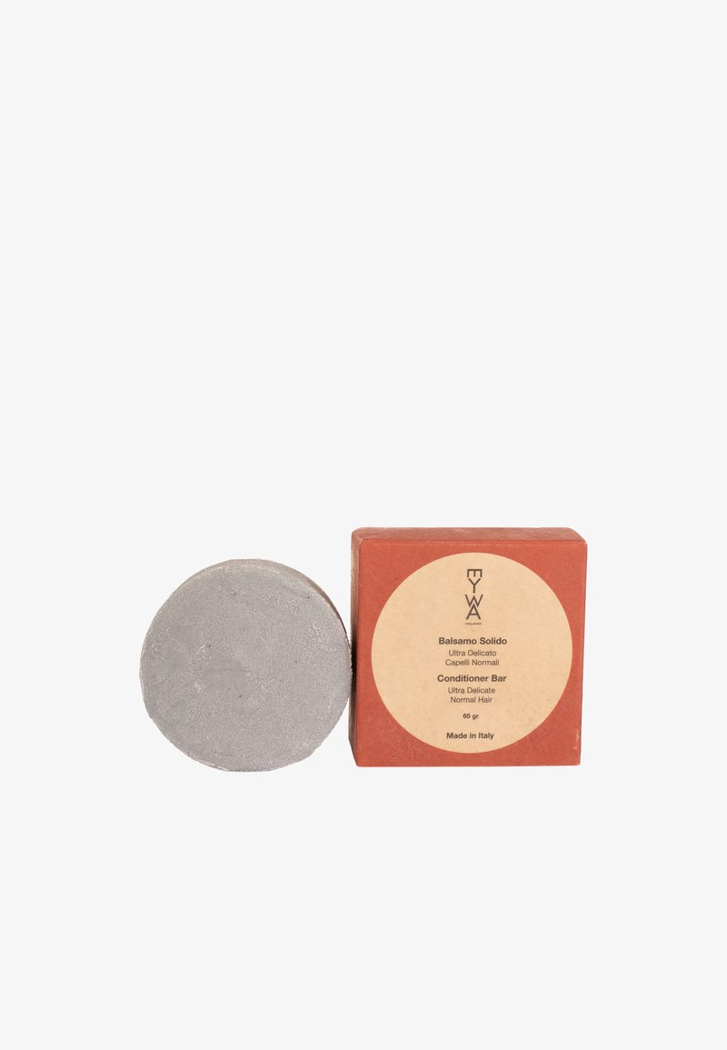 Balsamo solido in argento, con forma rotonda. Scatola di colore ruggine con un'etichetta circolare, che presenta i dettagli del prodotto in beige chiaro.