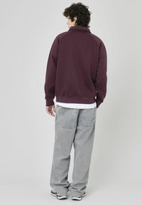 Pull bordeaux avec un col montant et des manches raglan, associé à un jean gris ample, doté de deux poches arrière et d'une finition texturée.