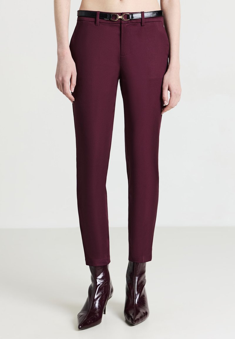 Burgunderfarbene Slim-Fit-Hosen mit einem glänzenden schwarzen Gürtel, der eine glatte Textur und taillierte Beine aufweist, akzentuiert durch eine goldfarbene Schnalle.