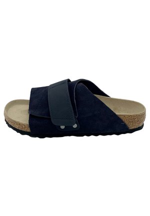 Black suede slide sandal with cork sole, adjustable strap over top, and textured black rubber outsole, side view.