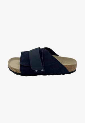 Black suede slide sandal with cork sole, adjustable strap over top, and textured black rubber outsole, side view.