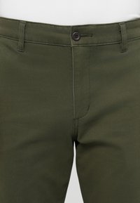 Olive green pants made of cotton blend fabric with a smooth texture, featuring a front button closure and standard pockets.