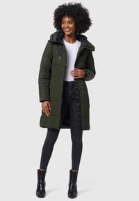 Groene pufferjack met capuchon, ritssluiting aan de voorkant en een gewatteerde textuur. Gecombineerd met zwarte skinny jeans en enkellaarzen, met een minimalistisch ontwerp.