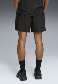 Sorte atletisk shorts med en glat tekstur, der har et tætsiddende design, længde over knæet, og parret med sorte sokker og sko.