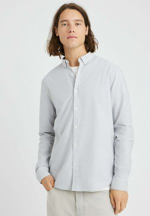 Chemise à rayures dans des tons de bleu clair et blanc, avec col, manches longues et coupe décontractée. Le tissu semble lisse avec une texture subtile.