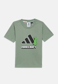 Zelena bombažna majica s kratkimi rokavi, ki ima črne Adidas stripe in grafiko Minecraft Creeper. Mehka tekstura, sproščen kroj.