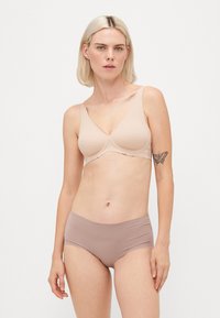 Light beige wireless bra with scalloped edge details and smooth cups, paired with seamless, mid-rise light brown panties.