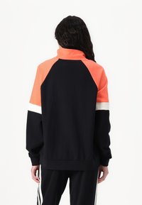 Felpa nera e corallo con colletto alto, maniche raglan e dettagli bianchi. Realizzata in tessuto morbido con una vestibilità comoda.