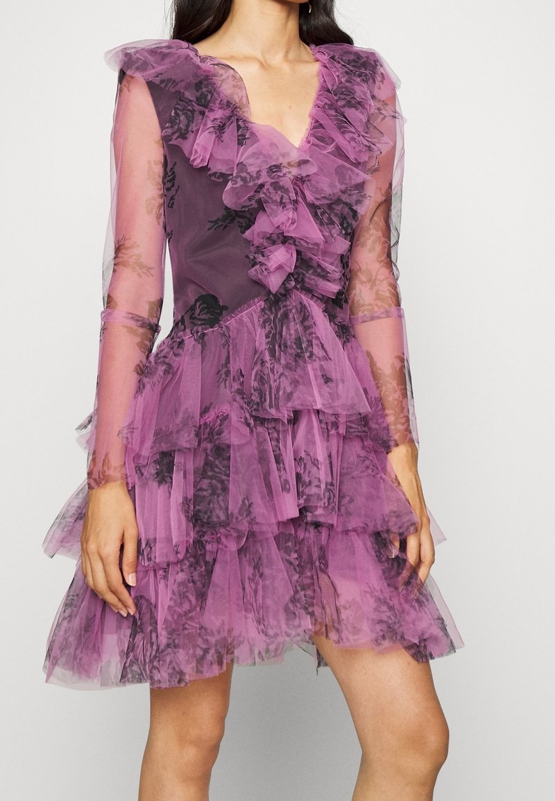 Vestido morado transparente con volantes y estampados florales negros, mangas largas y falda de tul en capas, llevado por una persona de pie.