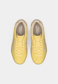 Κίτρινα σατέν αθλητικά παπούτσια με τρεις ανοιχτό μπεζ ρίγες, στρογγυλή μύτη, επίπεδα κορδόνια και μαλακή εσωτερική επένδυση με το λογότυπο Adidas στη γλώσσα.