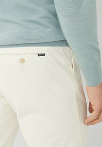 Hellblau gestrickter Pullover kombiniert mit cremefarbenen Chinos. Die Chinos haben einen Knopfverschluss und eine Gesäßtasche mit einem Markenlabel. Weiche Textur.
