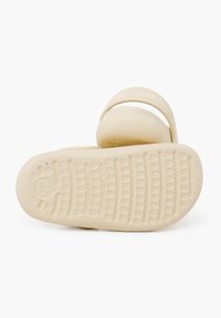 Sandal in plastica beige con suola texturizzata, cinturino largo e forma arrotondata. Presenta un design a impronta di zampa e la taglia 25 impressa sulla suola.