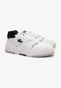 Hvite lær sneakers med svart tekstilkrage, rund tå og snøring. Har et side-logo og strukturert gummisåle.