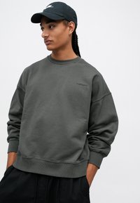 Süsimust sweatshirt ümarate kaelustega, sooniku vaheseinte ja allääriga. Esiküljel on vasakul rinnal peene logo. Pehme kangas, lõdva istuvusega.