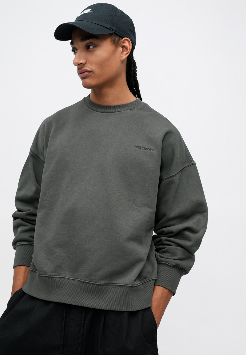 Sudadera gris carbón con cuello redondo, puños acanalados y dobladillo. Presenta un logo sutil en el lado izquierdo del pecho. Tejido suave, corte relajado.