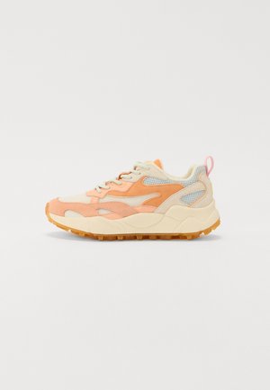 Les baskets présentent un mélange de mesh et de daim pêche et crème, des superpositions texturées, une épaisse semelle blanche et un accent rose sur le passant de talon.