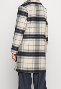 Rutig kappa i mjukt tyg, med en färgpalett av grädde, marinblå och beige, med synliga linjer och en avslappnad silhuett, medellång design.