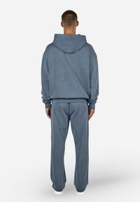 Grå hettegenser og matchende bukser laget av mykt stoff, med hette, avslappet passform og elastiske mansjetter ved ermer og ankler.