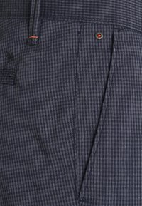 Pantaloni a quadri navy in un tessuto testurizzato, con una tasca frontale e un accento in bottone metallico di colore contrastante.