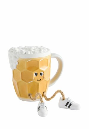 Yellow mug with foam on top, honeycomb pattern, smiling face with eyes, and rope legs wearing white sneakers.