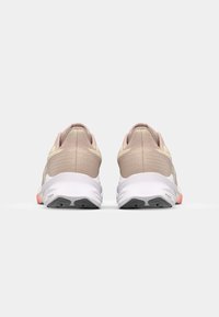 Sportieve schoenen met een zachte beige mesh bovenkant, textuuraccenten en een witte zool. De hak heeft een roze-oranje detail.