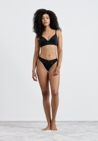 Zwart bikini set met een driehoekige bralette met dunne bandjes en een bijpassende low-rise brief. Gladde textuur, minimalistisch ontwerp.