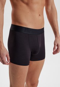 Schwarze Baumwoll-Boxershorts mit einem weichen, elastischen Bund, der ein geprägtes Branding aufweist, eng anliegendem Design und glatter Textur.
