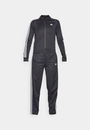 Tuta sportivo nero realizzato in tessuto liscio, caratterizzato da strisce bianche sulle maniche e sulle gambe, giacca con zip e pantaloni con vita elastica.