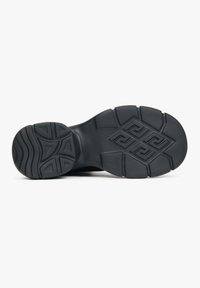 Black rubber shoe sole with textured tread pattern, featuring a geometric design and raised ridges for enhanced grip and traction.