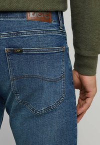 Jeans in denim blu con una finitura testurizzata, dotati di una toppa in pelle con il logo "Lee" in vita e un design di tasca posteriore curva.