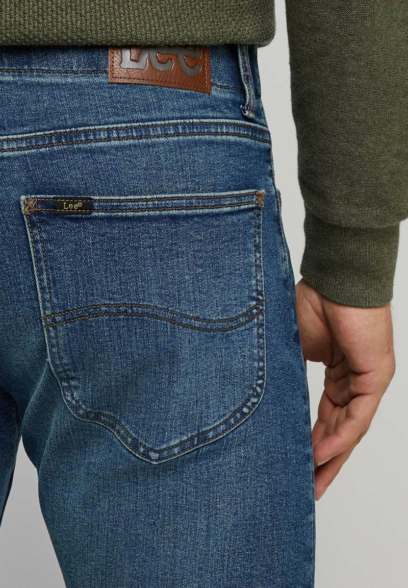 Niebieskie jeansy denimowe o teksturowanym wykończeniu, z skórzaną łatą z logo "Lee" w talii oraz zakrzywionym wzorem tylnej kieszeni.