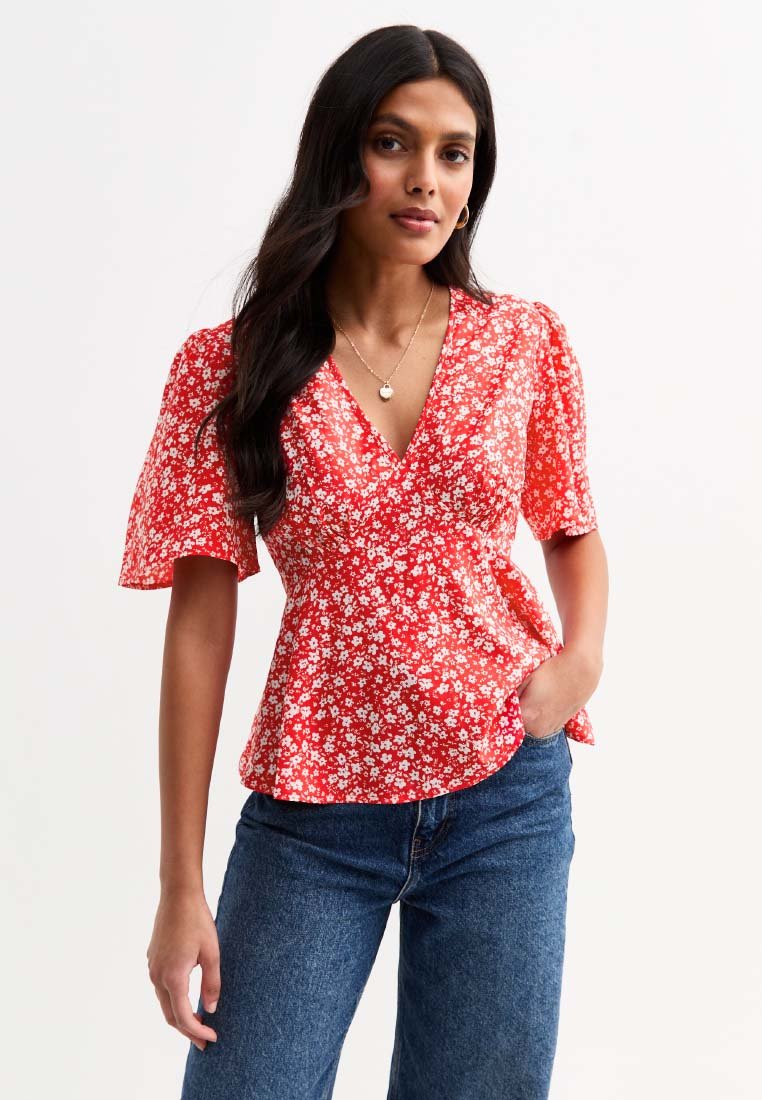 Red floral blouse with short, flared sleeves and a V-neckline. Lightweight fabric with white flower patterns, paired with blue denim jeans.