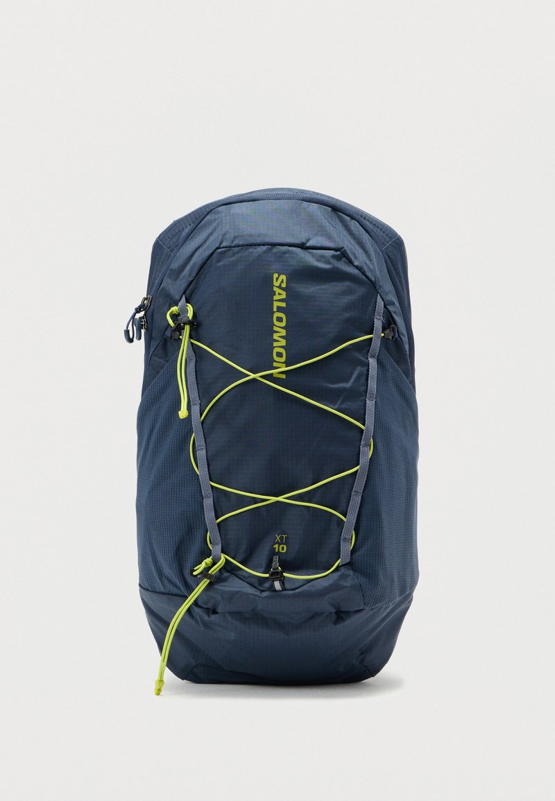 Το σακίδιο Salomon διαθέτει υφάσμα σκούρου μπλε με υφή, με φωτεινές κίτρινες λεπτομέρειες, σχεδίαση με ελαστικό κορδόνι και στρογγυλεμένο σχήμα για χρηστικότητα.