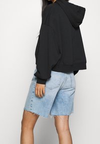 Černá krátká mikina s kapucí, doplněná světle modrými džínovými šortkami s třepícími se lemy. Šortky mají volný střih a zadní kapsy.