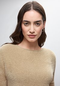 Beżowy, teksturowany sweter z dekoltem w łódkę. Miękki, puszysty materiał dopasowuje się do ciała, z subtelnym połyskiem i długimi rękawami.