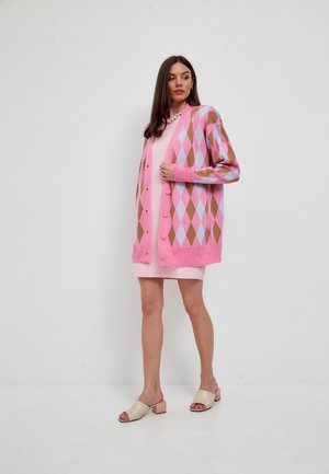 Roze cardigan met een ruitpatroon in lichtblauw en bruin, met knopen aan de voorkant. Draagt over een roze jurk, gecombineerd met beige sandalen.