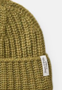 Un bonnet en tricot vert olive avec une texture côtelée et une étiquette cousue portant la mention "Marc O’Polo."