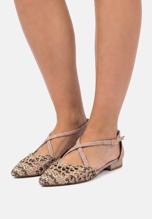 Piedi con ballerine beige intrecciate con punta affilata, cinturini intrecciati a incrocio sulla caviglia e una piccola fibbia su sfondo bianco.