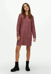 Abito di maglia in rosa tenue con maniche lunghe, trama a costine, motivi geometrici e silhouette dritta, abbinato a stivali neri alla caviglia.