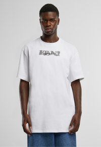 White cotton T-shirt with a loose fit, featuring a gray graphic design that reads "KANYE" across the chest. Short sleeves, round neckline.