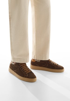 Sneaker in pelle scamosciata marrone con lacci in cotone testurizzato, suole in gomma e dettagli beige, indossati con pantaloni chiari e di taglio largo.