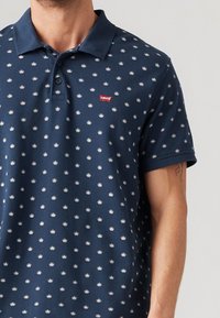 Polo din bumbac de marină, realizat dintr-un material texturat, cu un model mic de coroane și un logo Levi's roșu în partea stângă a pieptului. Mâneci scurte.