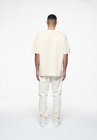 T-shirt crema a maniche corte abbinata a pantaloni chiari, entrambi realizzati in tessuto morbido, con una vestibilità comoda e un design semplice.