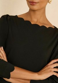 Mustmustega, millel on laineline kaelus ja mansetid. Sile kangas, lähedane hõlmamine, käed risti, et näidata lähedalt.