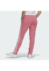 Rosa sweatpants med vita sidosträck, elastisk midja och fotledsmuddar. Slät tyg med avslappnad passform. Bärs med vita sneakers.