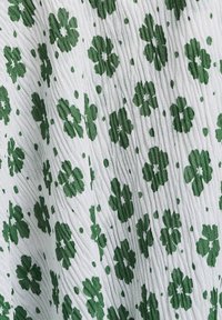 Tela con estampado floral que presenta flores verdes sobre un fondo blanco, con un diseño texturizado y plisado y pequeños acentos verdes en todo su recorrido.