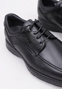Scarpe in pelle nera con una superficie liscia, design con lacci e leggera imbottitura sulla suola. Presentano cuciture sottili e un dettaglio con logo.