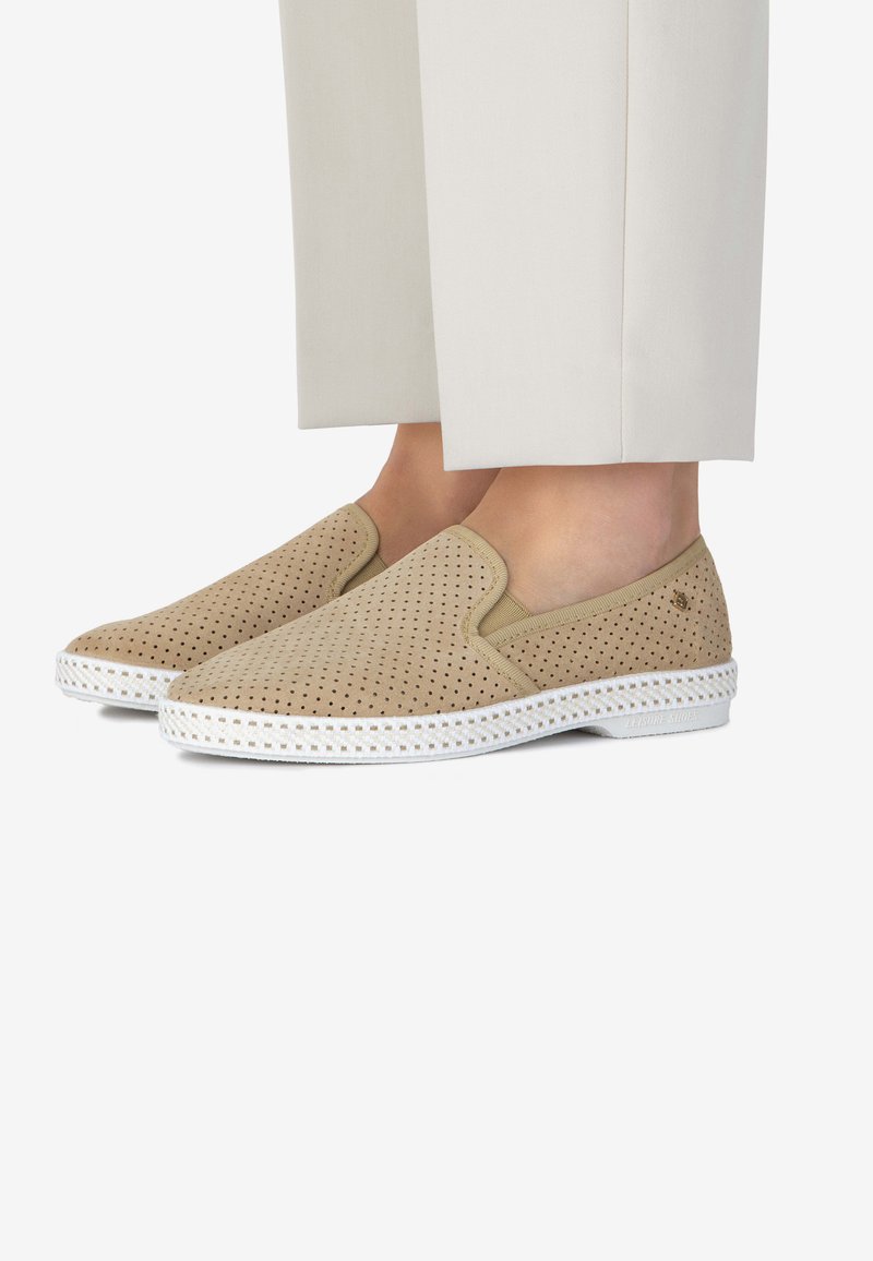 Beige instap schoenen van geperforeerd materiaal met een witte rubberen zool en accentstiksels. Gladde textuur met elastische zijpanelen.